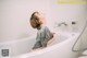 A woman taking a bath in a white bathtub.