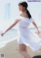 A woman in a white dress walking on the beach.