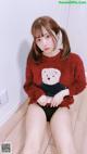 a woman sitting on the floor wearing a red sweater and black panties