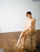 A naked woman sitting on a wooden floor in a sheer dress.