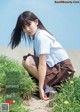 A young woman in a school uniform crouching down in the grass.