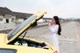 A woman in a white dress standing next to a yellow car.